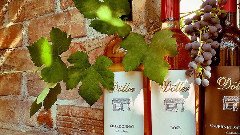 Three Döller wine bottles in front of a brick wall with vine leaves and grapes.
