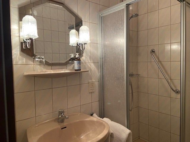 A bathroom with washbasin, mirror, shower and towel.