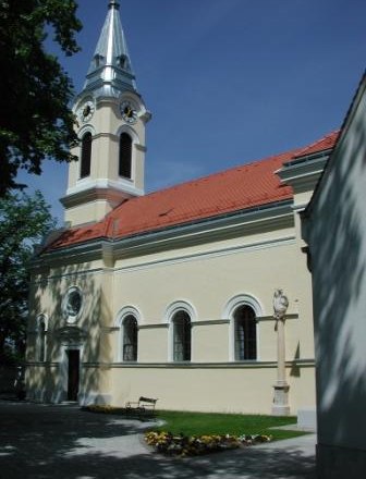Tattendorf parish church with yellow fa&ccedil;ade and red roof, surrounded by trees.
