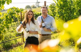 Two people holding bottles of wine in a vineyard.