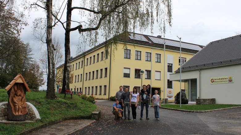 Group of people in front of a yellow school building with solar panels on the roof.