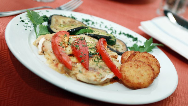 A plate of roasted vegetables, tomatoes and rösti on a red table.