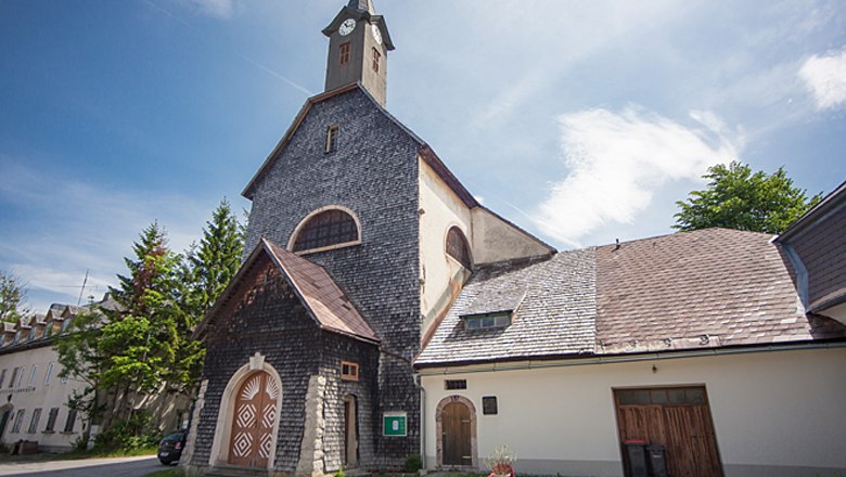 Josefsberg parish church with stone-clad façade and tower under a blue sky.