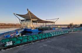Open-air stage with empty rows of seats on the riverbank at sunrise.