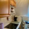 Small kitchen with wooden cupboards, stove, coffee machine and open fridge.