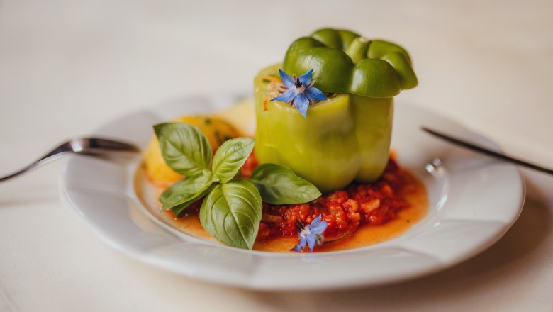 Stuffed green bell pepper on tomato sauce, garnished with basil and blue blossom on a white plate.