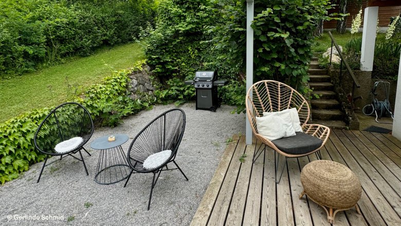 Terrace with glass roof, garden furniture and barbecue, surrounded by green vegetation.