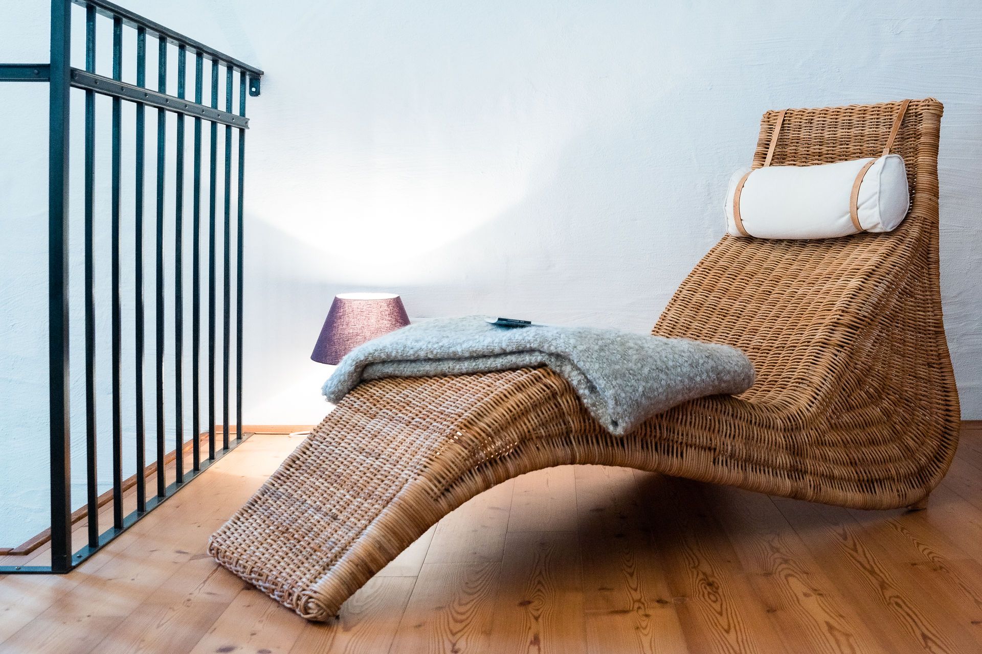 A cozy reading corner with a woven deck chair, a blanket and a lamp on a wooden floor.