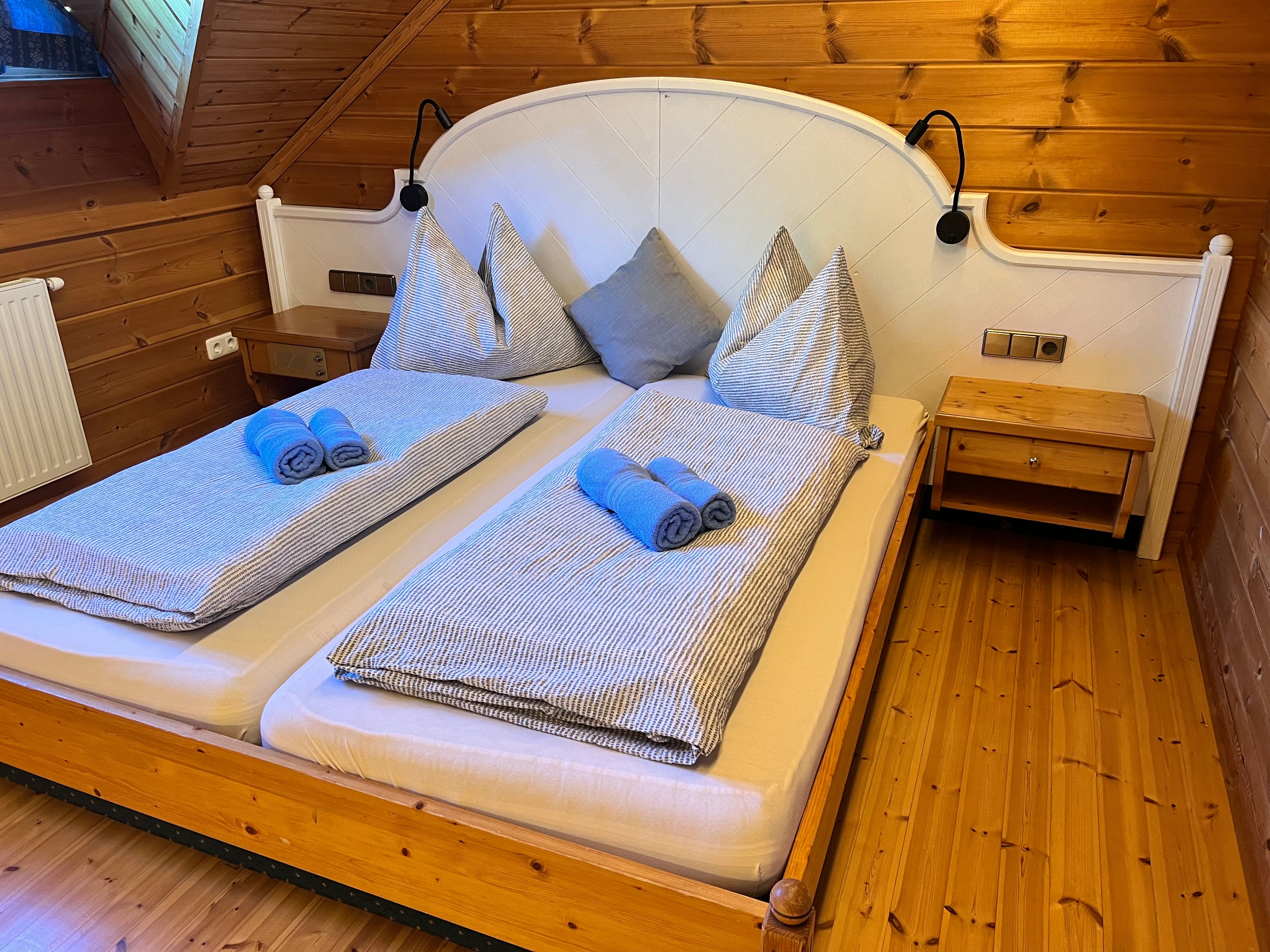A cozy bedroom with wooden walls and a double bed decorated with blue towels and striped bedding.