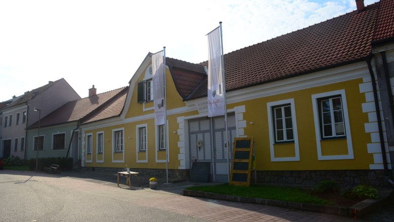 Yellow building with red roof tiles and two flags in front of it.