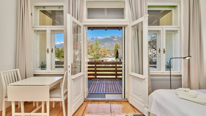 Interior with wooden floor, table, chairs and view of the balcony and mountains.