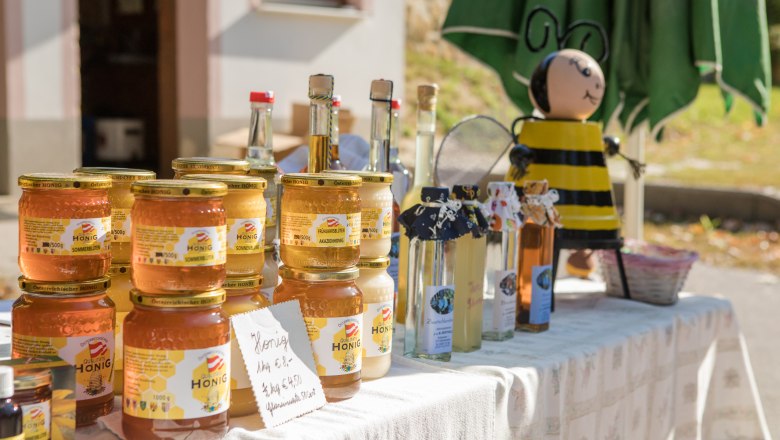 Honey jars and bottles on a table with a bee figure in the background.