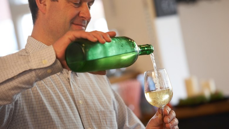 A man pours white wine from a green bottle into a glass.