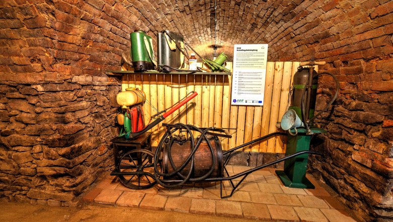 Historical agricultural equipment on display in a vaulted cellar.