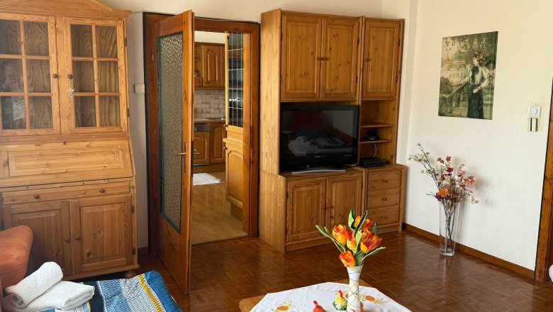 Living room with wooden furniture, a table with flowers and a TV.