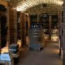 A wine cellar with a vaulted ceiling, wine bottles on shelves and a barrel in the middle.