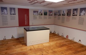 Interior view of an exhibition on fortified church documentation with information boards and a display table.