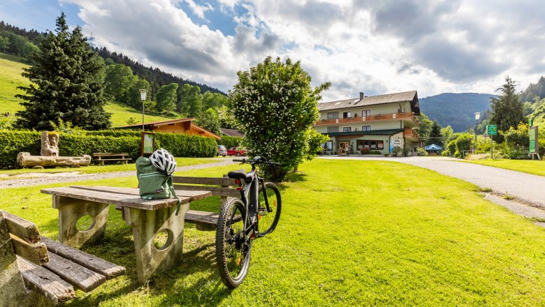A bicycle is parked next to a picnic table on a green meadow in front of a building called Hubertushof.