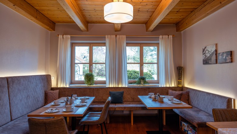 Cozy dining area with wooden beamed ceiling, window and set table.