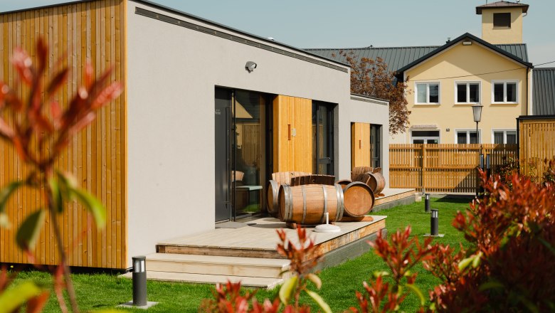 Ipsmiller Apartments, © Michael Reidinger Modern apartments with wood paneling and wine barrels on the terrace, surrounded by green lawns and a fence.