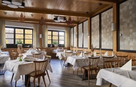 An elegant restaurant with wooden furniture, white tablecloths and large windows showing autumnal trees.