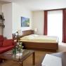 Cozy hotel room with double bed, red sofa, glass table and decorations.