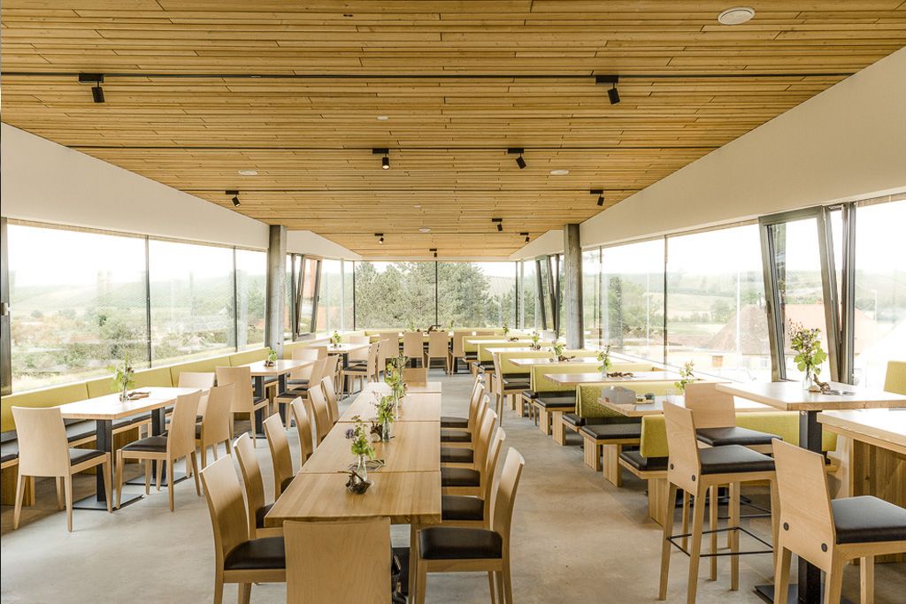 Interior view of a modern restaurant with wooden furniture and large windows.