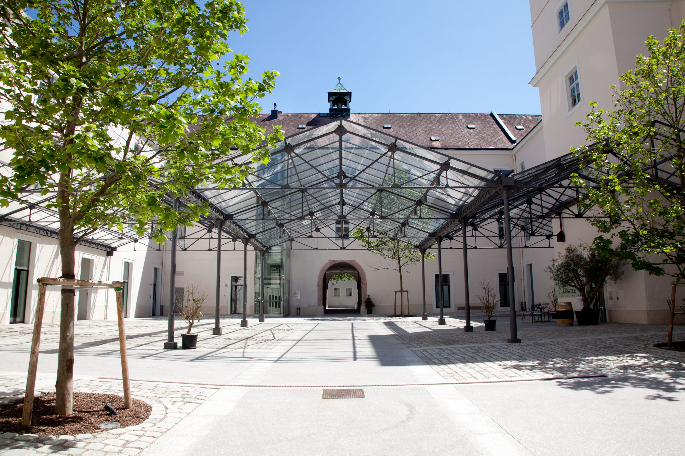 Inner courtyard with glass roof and trees, surrounded by buildings.