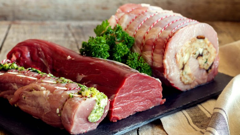 Various pieces of meat on a wooden board, decorated with herbs.