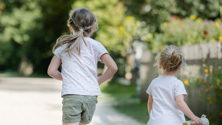 Two children running on a gravel path in a green park.