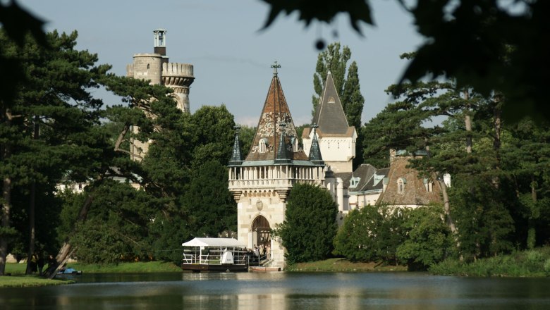 Laxenburg Castle with towers and trees on the lakeshore.