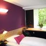 Modern furnished room with purple wall, bed, desk and window with a view of the greenery.