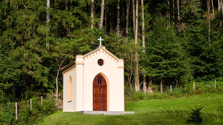 A small chapel with a cross on the roof, surrounded by trees and grass.