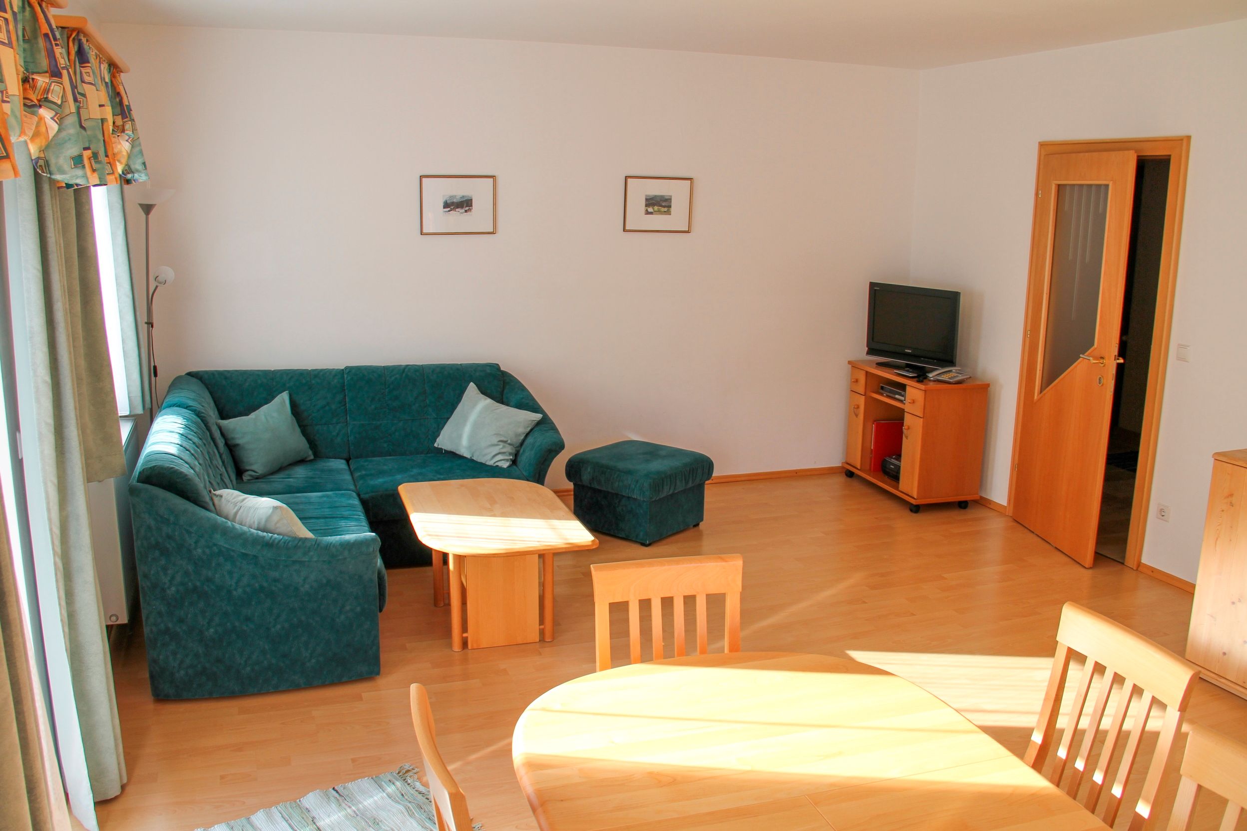 Living room with green corner sofa, wooden table, TV and dining table.