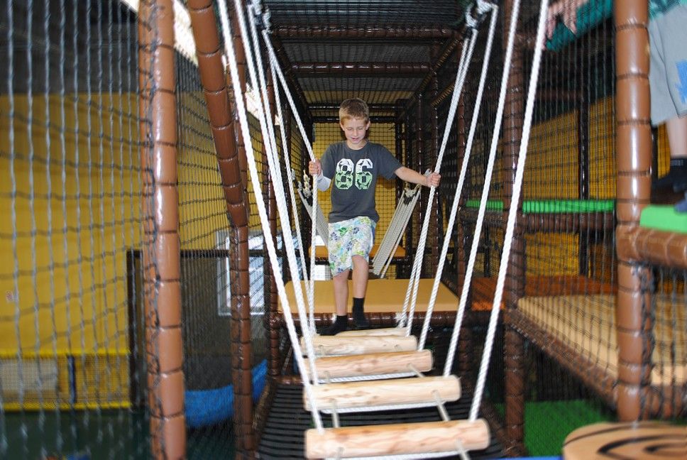 A boy balances on a suspension bridge in an indoor climbing garden.