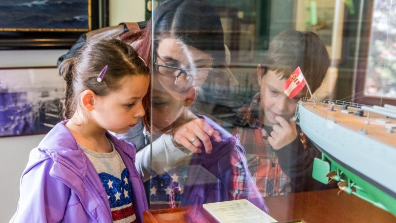 Children look at a model ship in a museum.
