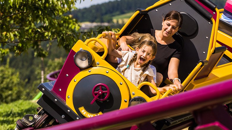 A woman and a child in the carriage of a roller coaster in the Eis-Greissler adventure park.