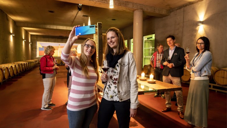 People take a selfie in a wine cellar with barrique barrels.