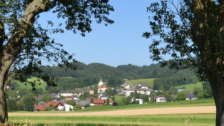 Landscape with village and church in the background, framed by trees.