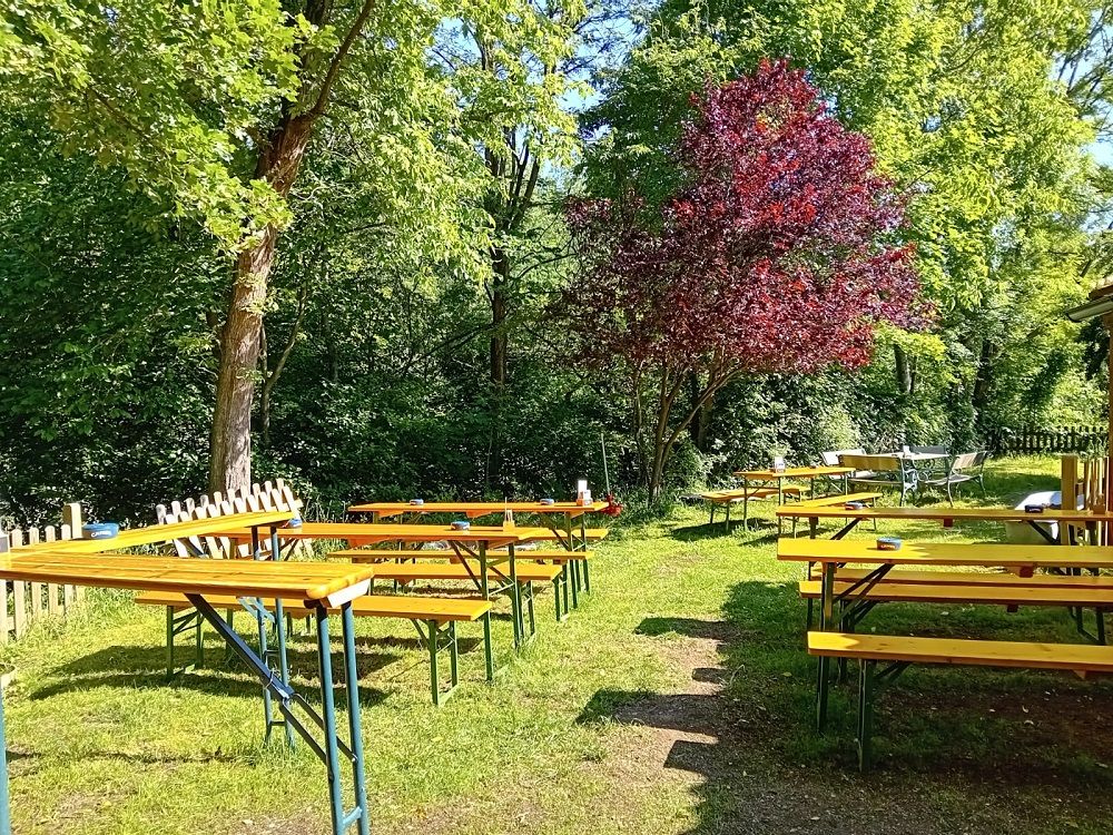 A beer garden with empty wooden benches and tables under trees.
