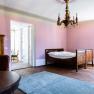 An elegant room with pink walls, a wooden bed, a chandelier and a carpet on a wooden floor.