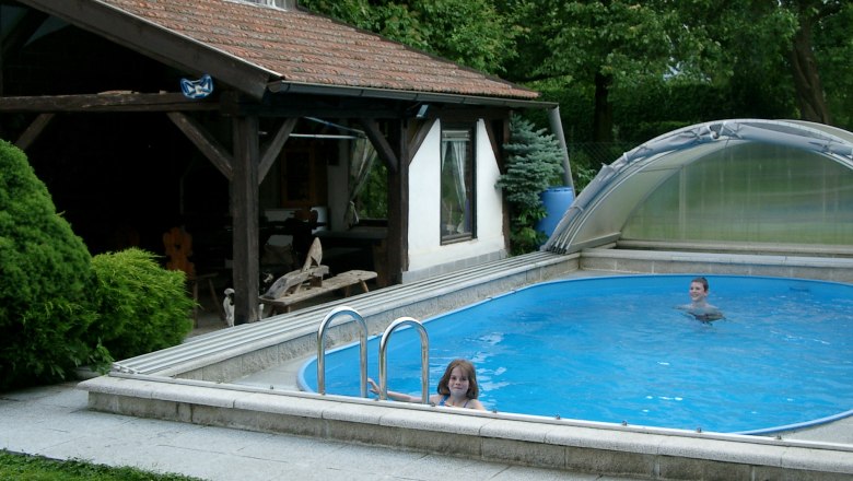 Two children swim in a small, covered pool next to a wooden pavilion.