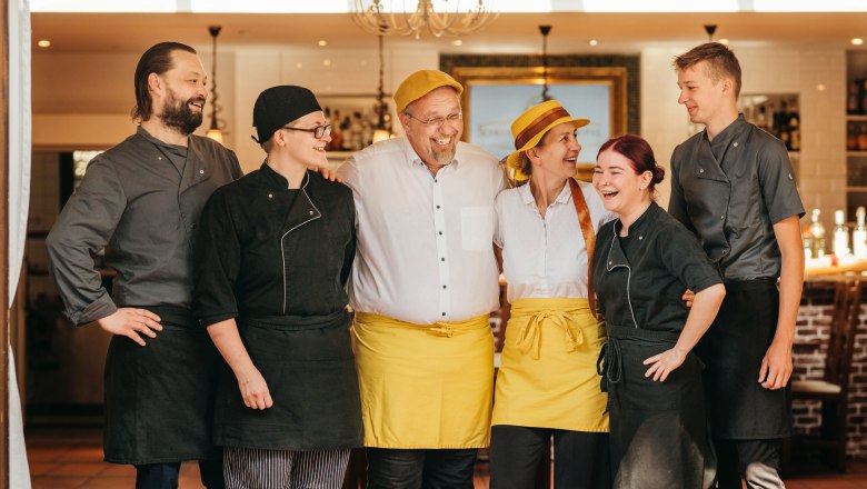 A cheerful team of six people in work clothes stands smiling in a restaurant.