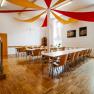 A bright dining room with a wooden floor, tables and chairs. Red and yellow fabric panels hang from the ceiling.