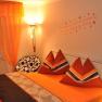 Cozy bedroom with orange bed linen and curtains, decorative cushions and wall tattoo.