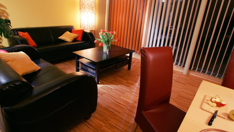 Cozy living room with leather sofas, coffee table, bouquet of flowers and dining table with fruit.