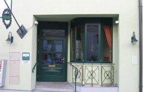 Entrance area of a building with green door and windows, decorated with plants and lanterns.
