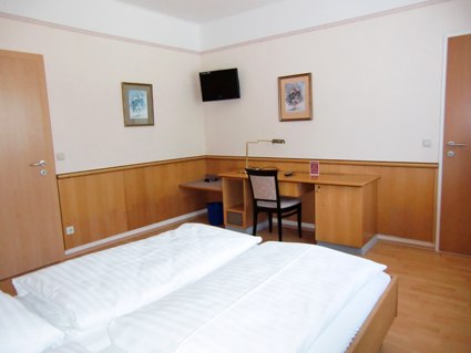A hotel room with double bed, desk, chair and wall decoration.