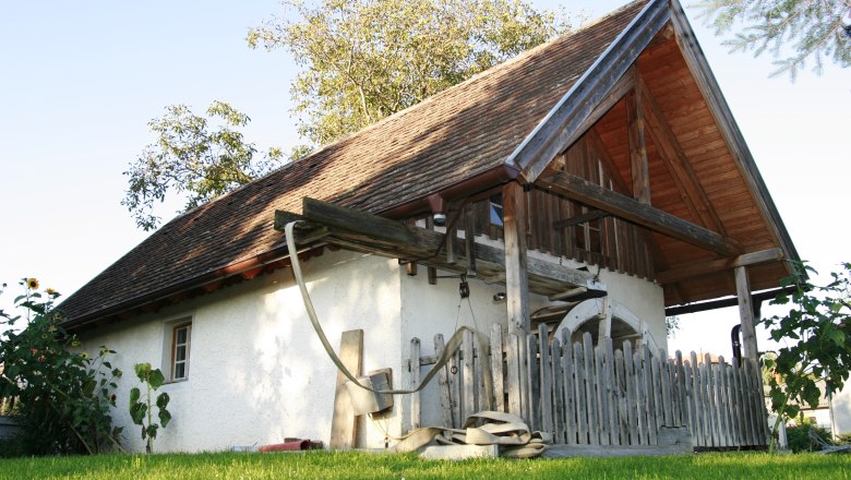 Traditional building with wooden roof and fence, surrounded by green meadow and trees.