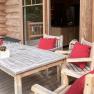 Wooden terrace with table and chairs, red cushions and a dog in the background.